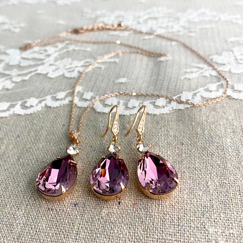 Puede incluir: Un conjunto de joyas que incluye un collar y pendientes. El conjunto presenta un collar de cadena de oro rosa con un colgante en forma de l&aacute;grima de color p&uacute;rpura oscuro. Los pendientes tienen un dise&ntilde;o similar, con una piedra p&uacute;rpura en forma de l&aacute;grima y ganchos dorados.