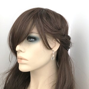 May include: Silver-toned drop earrings featuring clear, teardrop-shaped crystals. The earrings are displayed on a mannequin with brown hair and a fair complexion. The earrings have a small, decorative clasp.