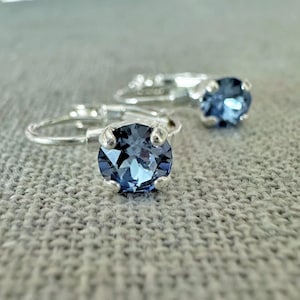May include: A pair of silver-toned leverback earrings, each featuring a single round, faceted dark blue crystal stone held in a four-prong setting. The earrings are designed with a secure hinged closure mechanism for attachment to the earlobe.
