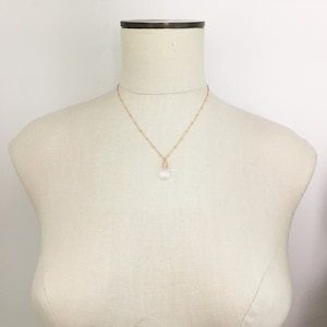 May include: A delicate rose gold necklace with a small, clear crystal pendant. The necklace features a fine chain with small, evenly spaced beads. The crystal pendant is faceted, catching the light. The necklace is displayed on a mannequin.