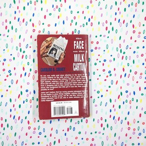 May include: A paperback book titled "The Face on the Milk Carton" by Caroline B. Cooney. The cover is red with a photo of a missing person flyer. The book is set against a white background with colorful, abstract shapes.