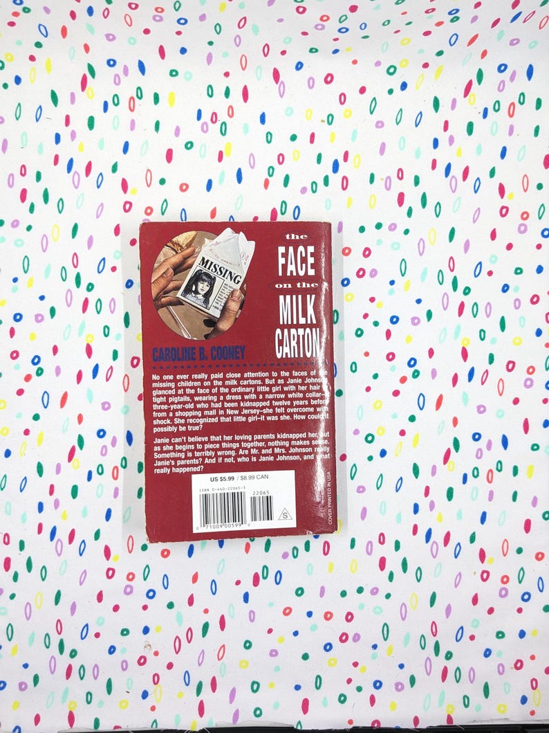 May include: A paperback book titled "The Face on the Milk Carton" by Caroline B. Cooney. The cover is red with a photo of a missing person flyer. The book is set against a white background with colorful, abstract shapes.