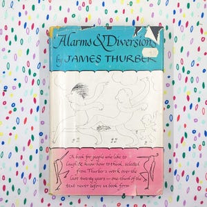 May include: A pink and white book cover with the title "Alarms & Diversions" by James Thurber. The cover features a black and white illustration of three people walking.