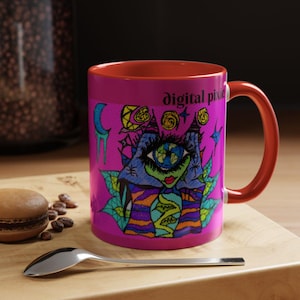 Puede incluir: Taza de cerámica magenta con interior y asa rojos. La taza presenta una ilustración colorida y caprichosa con el texto "digital pixie". El diseño incluye un ojo, estrellas y otros elementos abstractos. La taza está sobre una superficie de madera.