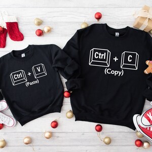 May include: Two black sweatshirts with white text and images of computer keys. The larger sweatshirt says "Ctrl + C (Copy)" and the smaller sweatshirt says "Ctrl + V (Paste)".