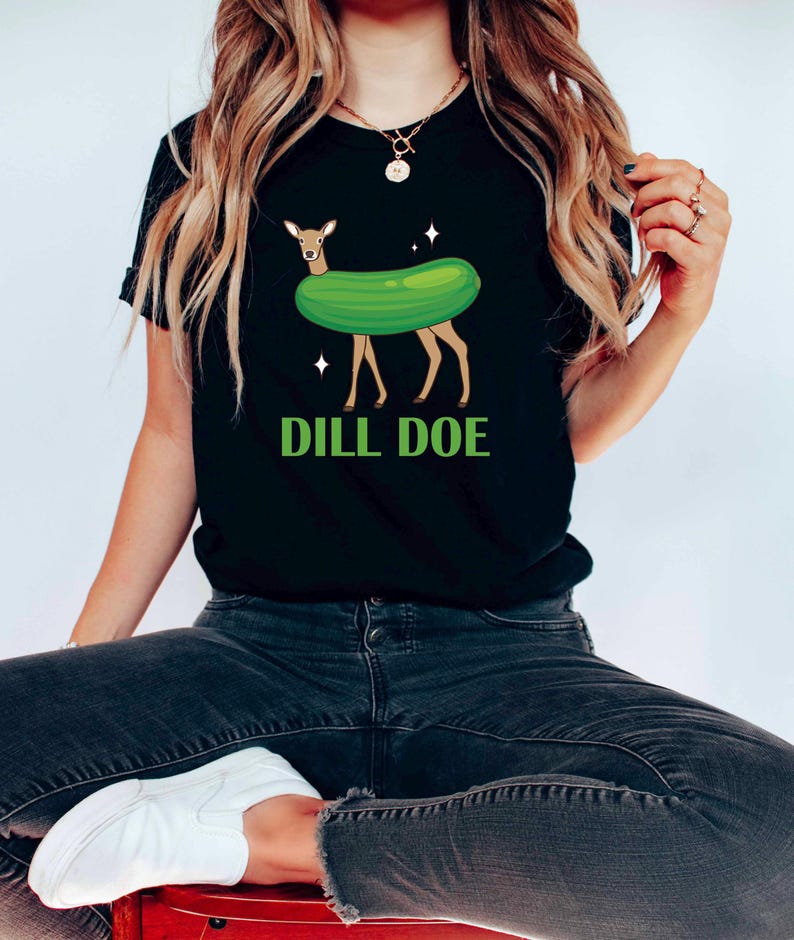 Puede incluir: Camiseta negra con un ciervo verde en forma de pepinillo y el texto "DILL DOE" en letras verdes.
