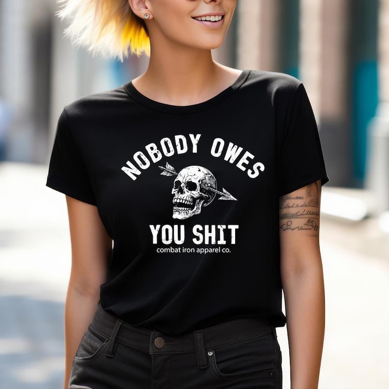 May include: Black t-shirt with the text "NOBODY OWES YOU SHIT" in white, along with a skull pierced by an arrow. The shirt also features the text "combat iron apparel co." at the bottom.