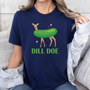 Puede incluir: Una camiseta azul marino con una imagen de dibujos animados de un ciervo con un disfraz de pepinillo. El texto "DILL DOE" est&aacute; impreso debajo de la imagen.