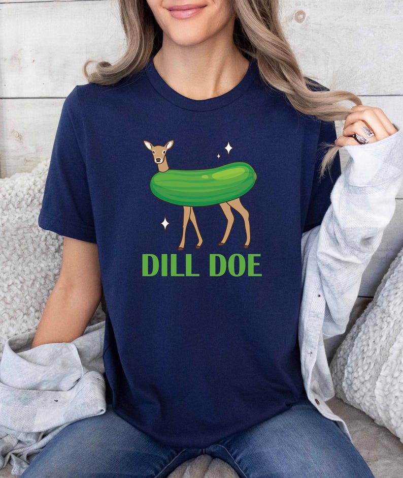 Puede incluir: Una camiseta azul marino con una imagen de dibujos animados de un ciervo con un disfraz de pepinillo. El texto "DILL DOE" est&aacute; impreso debajo de la imagen.