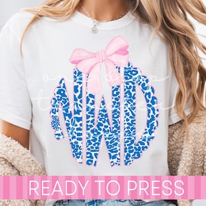 May include: White t-shirt featuring a pink bow and the letters "NWD" in a blue leopard print design. The text "READY TO PRESS" is displayed in a pink banner across the bottom. The shirt is a casual style.