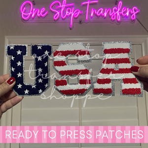May include: A set of three chenille patches spelling USA. The U is dark blue with white stars, while the S and A feature red and white horizontal stripes. Each letter has a silver glitter border. The text One Stop Transfers is visible.
