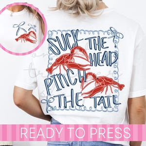 May include: White t-shirt with a red crawfish graphic and the text "Suck the Head, Pinch the Tail" in blue. The shirt also features a small crawfish graphic on the front.