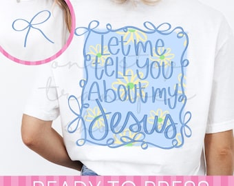 May include: A white t-shirt featuring a light blue rectangular background with yellow daisy flowers and the blue cursive text Let me tell you About my JESUS. The design is framed by a blue line border with decorative loops at the corners.