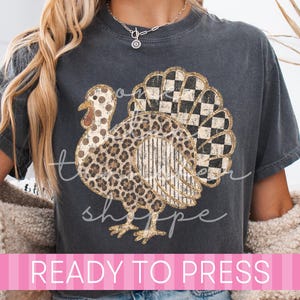 May include: A charcoal gray t-shirt featuring a graphic of a turkey with a multi-patterned design. The turkey body has leopard print, polka dots, vertical stripes, and a black and white checkered tail. The text READY TO PRESS is visible.