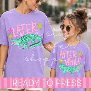 May include: Two lavender t-shirts with matching designs. Each shirt features a green alligator graphic and text that reads "LATER" and "AFTER WHILE" in pink. The shirts are ready to press.