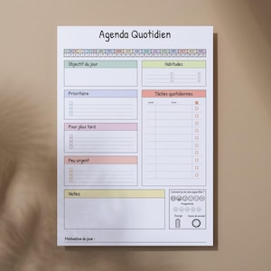 May include: A white daily planner with the title "Agenda Quotidien" at the top. It features sections for daily objectives, habits, tasks, and notes, with a color-coded layout. The planner is designed for daily use.
