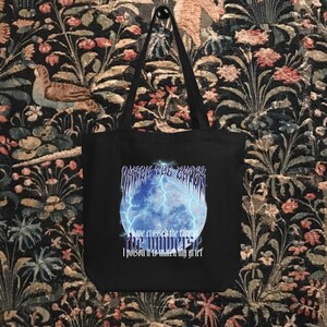 May include: Black tote bag with a graphic of a blue planet with lightning bolts and the text "WRECK THE GARDEN WITHIN THE GHETTO" and "I have crossed the face of the universe, I poison it to match my grief".