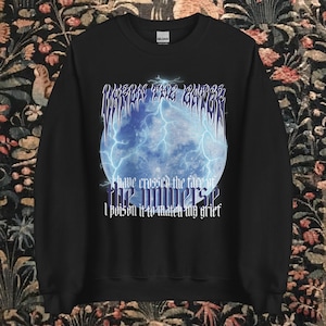 May include: Black sweatshirt with a blue and white graphic of a moon with lightning bolts and text that reads "I have crossed the face of the universe. I poison it to watch my grief."
