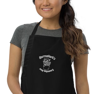 May include: Black apron with a white embroidered design of a cauldron with a skull and crossbones and the text "Sarrowhark's Soup Dispensary".