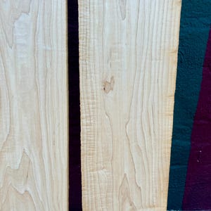 May include: Two pieces of light brown wood with a natural grain pattern. The wood is smooth and has a light sheen. The wood is likely maple.