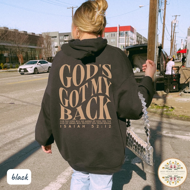 May include: Black hoodie with the text "GOD'S GOT MY BACK" in a tan color on the back. The hoodie also features the Bible verse Isaiah 52:12. The hoodie is a casual apparel item.