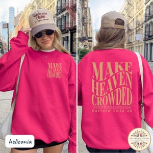 May include: A bright pink long-sleeve sweatshirt featuring the text "MAKE HEAVEN CROWDED" in a wavy gold font on the back, with a smaller version on the front left chest. The back also includes the scripture Matthew 28:19-20 in small gold text.