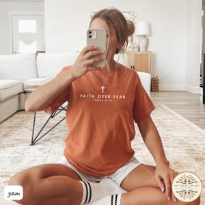 May include: A rust-colored t-shirt with a white cross and the text "Faith Over Fear Isaiah 41:10".