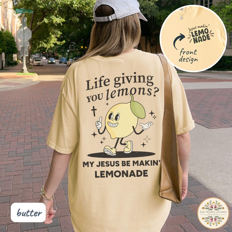 May include: Butter-colored t-shirt with a cartoon lemon design and the text "Life giving you lemons? My Jesus be makin' lemonade." The front design says "Jesus makin' lemonade."