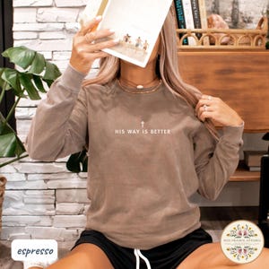 May include: Espresso-colored long-sleeve shirt with the text "HIS WAY IS BETTER" and a cross graphic. The shirt is a neutral color and has a relaxed fit. The shirt is part of the Red Prairie Apparel collection.