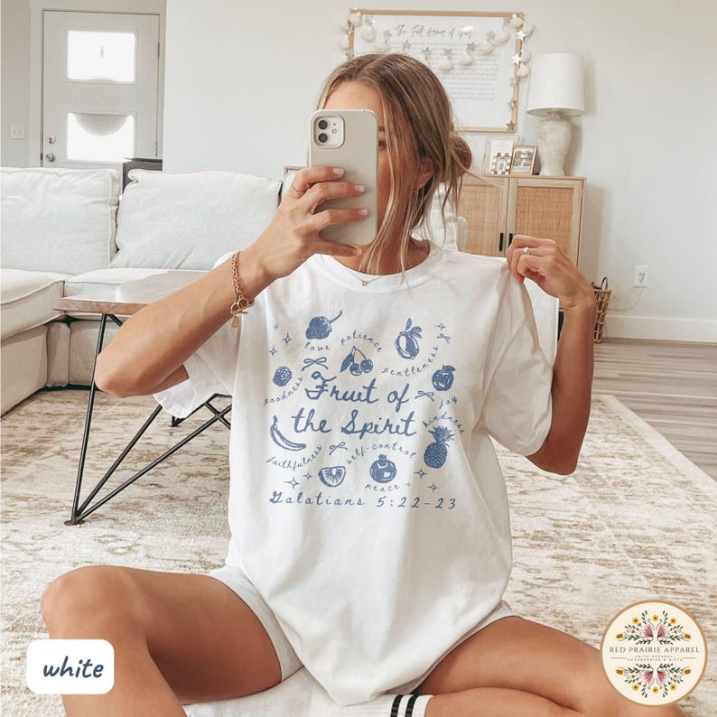 May include: White t-shirt with a blue graphic design featuring the text "Fruit of the Spirit" and various fruit illustrations. The text "Galatians 5:22-23" is also included. The shirt is from Red Prairie Apparel.