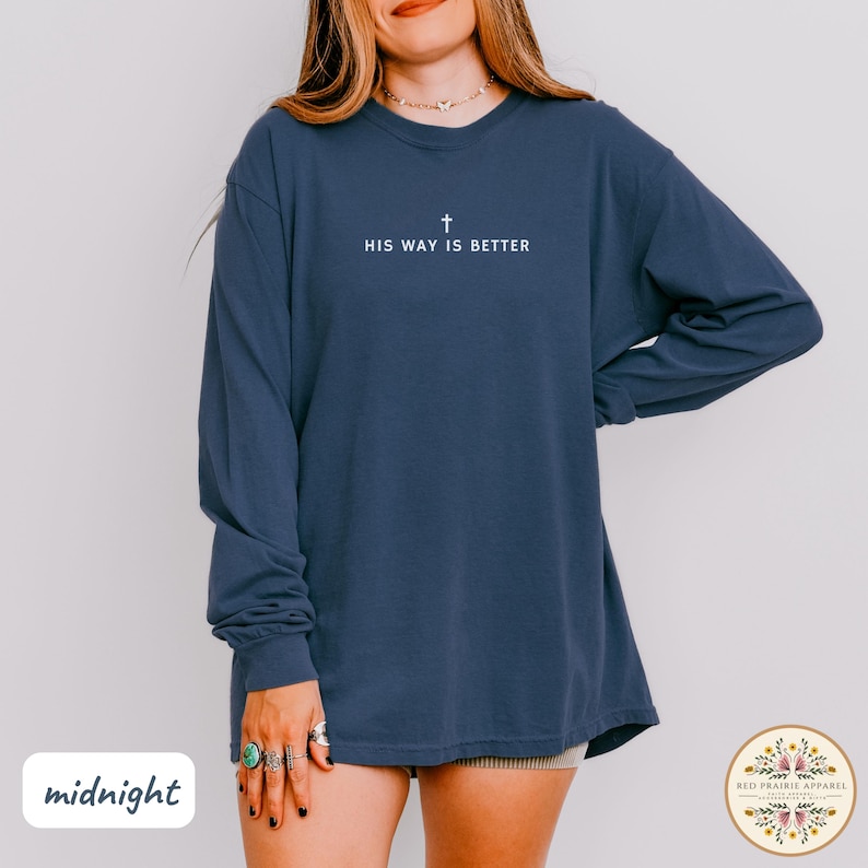 May include: A navy blue long-sleeve shirt with the text "HIS WAY IS BETTER" and a cross symbol in white. The shirt is a relaxed fit and has a crew neck. The word "midnight" is in the lower left corner.