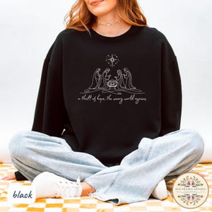 May include: Black sweatshirt featuring a white line drawing of the Nativity scene with a star above. The text "a thrill of hope, the weary world rejoices" is below the image. The word "black" is at the bottom left.