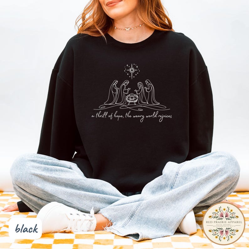 May include: Black sweatshirt featuring a white line drawing of the Nativity scene with a star above. The text "a thrill of hope, the weary world rejoices" is below the image. The word "black" is at the bottom left.