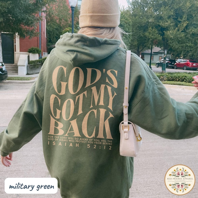 May include: Military green hoodie with the text "GOD'S GOT MY BACK" in a tan color. The hoodie also features a quote from Isaiah 52:12. The hoodie is part of the Red Prairie Apparel collection.