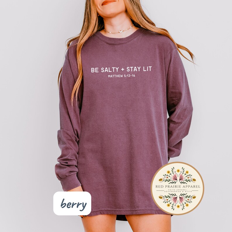 K&ouml;nnte beinhalten: Ein lang&auml;rmeliges, beerfarbenes Shirt mit dem Text "BE SALTY + STAY LIT" und "MATTHEW 5:13-16" in Wei&szlig;. Das Shirt hat einen Rundhalsausschnitt und ist aus einem weichen, bequemen Stoff gefertigt.