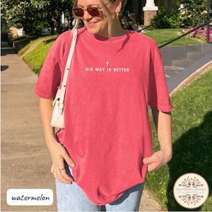 May include: A watermelon-colored t-shirt with the text "HIS WAY IS BETTER" and a small cross above the text. The shirt is a short-sleeved, crew neck style. The bottom left corner of the image has the word "watermelon".