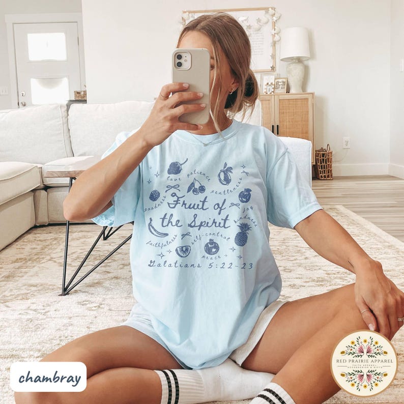 May include: Light blue t-shirt with the text "Fruit of the Spirit" and illustrations of various fruits. The text "Galatians 5:22-23" is also printed on the shirt. The shirt is labeled "chambray" and has a Red Prairie Apparel logo.