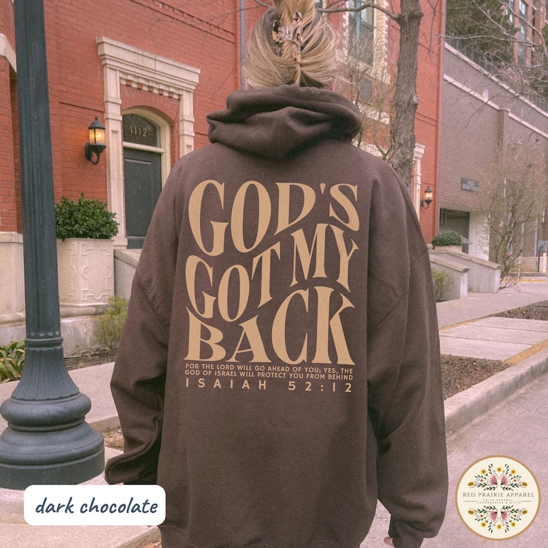 May include: Dark chocolate brown hoodie with the text "GOD'S GOT MY BACK" in a tan color on the back. The hoodie also features the Bible verse Isaiah 52:12. The hoodie is a comfortable, casual style.