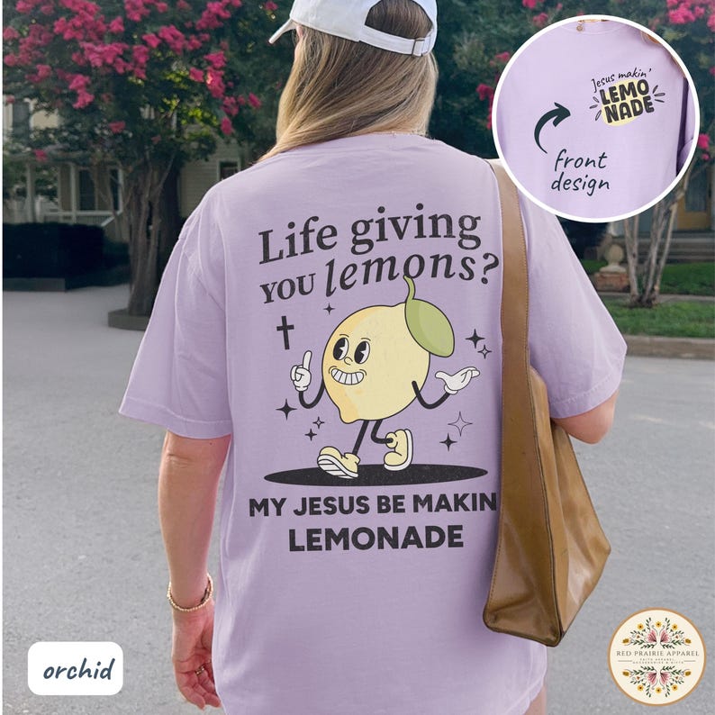 May include: Orchid-colored t-shirt with a cartoon lemon graphic and the text "Life giving you lemons? My Jesus be makin lemonade." The front design reads "Jesus makin' lemonade."