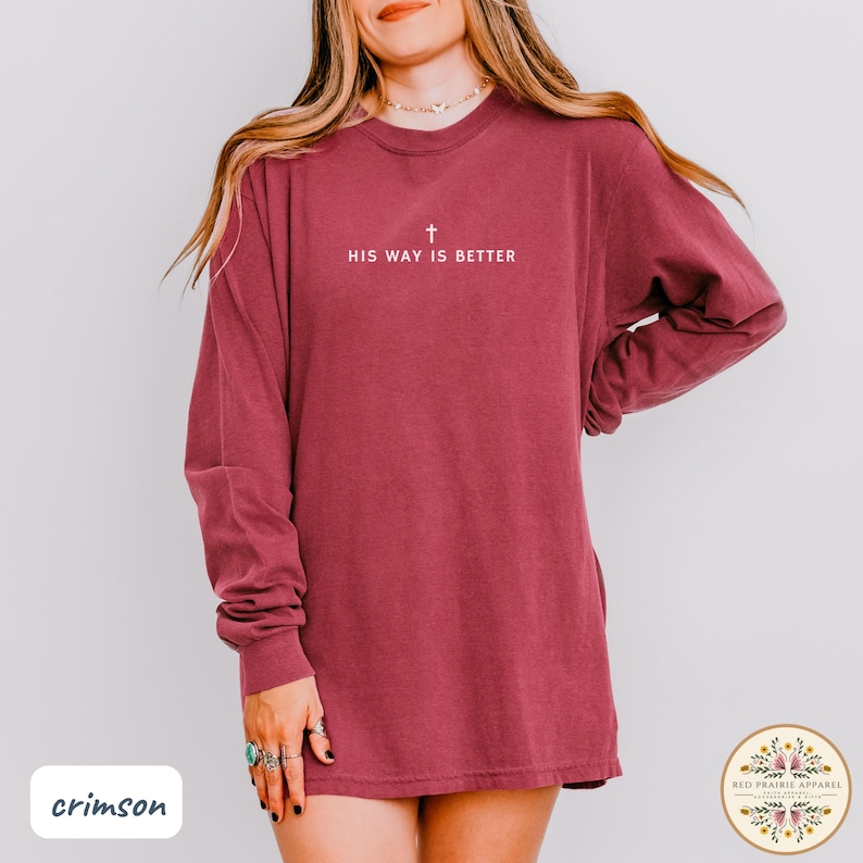 May include: Crimson long-sleeve shirt with the text "HIS WAY IS BETTER" and a cross symbol in white. The shirt is a solid crimson color and has a relaxed fit. The shirt is from Red Prairie Apparel.