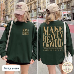 May include: A forest green long-sleeve sweatshirt featuring the text "MAKE HEAVEN CROWDED" in gold on the front left chest and a larger version on the back with the scripture "MATTHEW 28:19-20" printed below in gold lettering on the back.