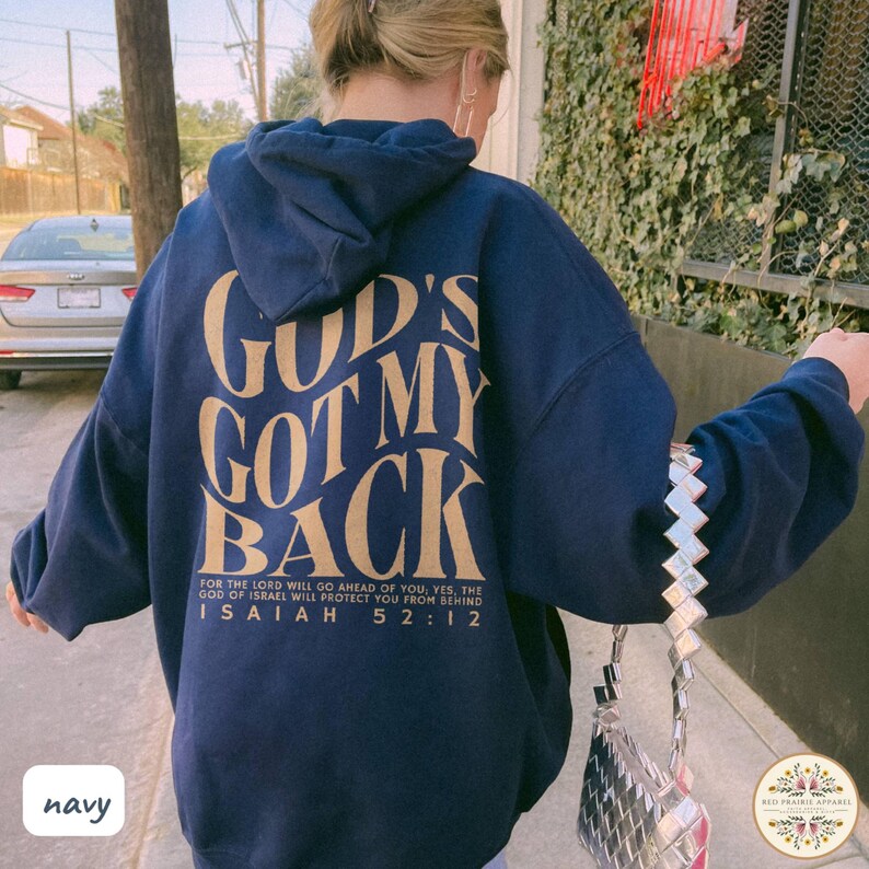 May include: Navy blue hoodie with the text "GOD'S GOT MY BACK" in a gold color on the back. The hoodie also features the Bible verse Isaiah 52:12. The hoodie is a comfortable, casual style.