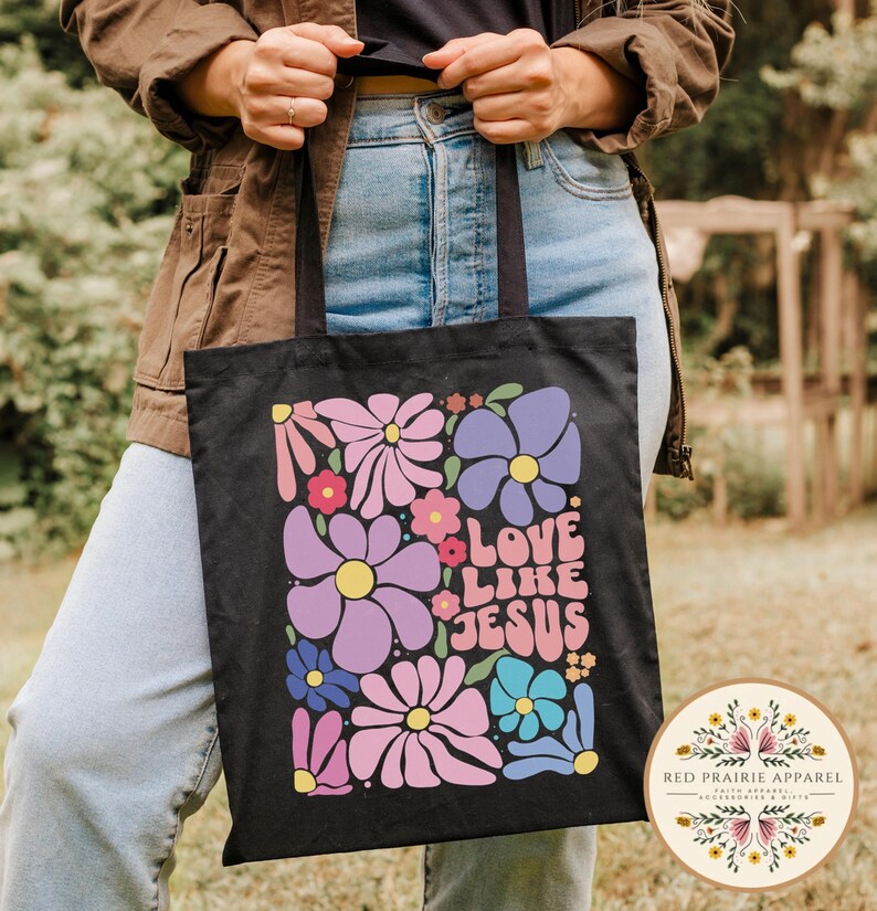 May include: Black canvas tote bag with a floral design and the text "Love Like Jesus" in colorful letters.