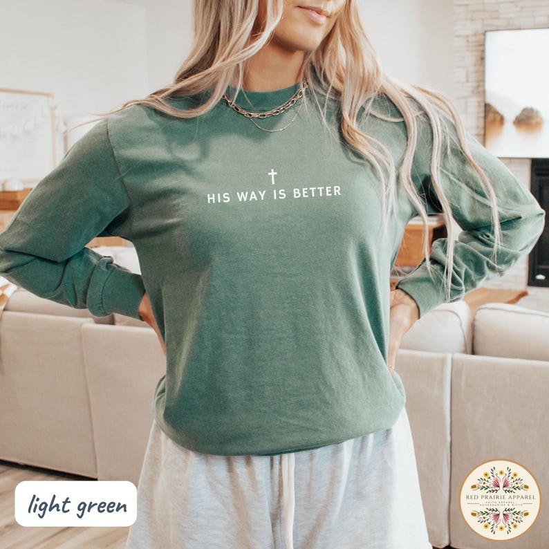 May include: A light green long-sleeve shirt with the text "HIS WAY IS BETTER" and a cross graphic. The shirt is a solid color and has a crew neck. The shirt is made of a soft material.