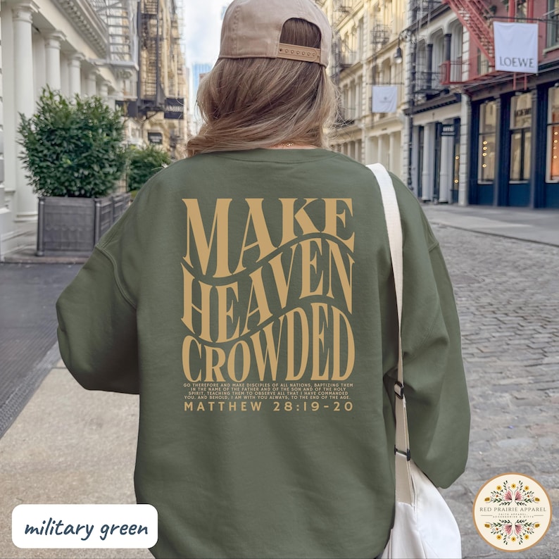 May include: An olive green crewneck sweatshirt featuring the text "MAKE HEAVEN CROWDED" in large, wavy, tan-colored letters on the back. Below the main text, smaller print reads "GO THEREFORE AND MAKE DISCIPLES OF ALL NATIONS" and "MATTHEW 28:19-20".