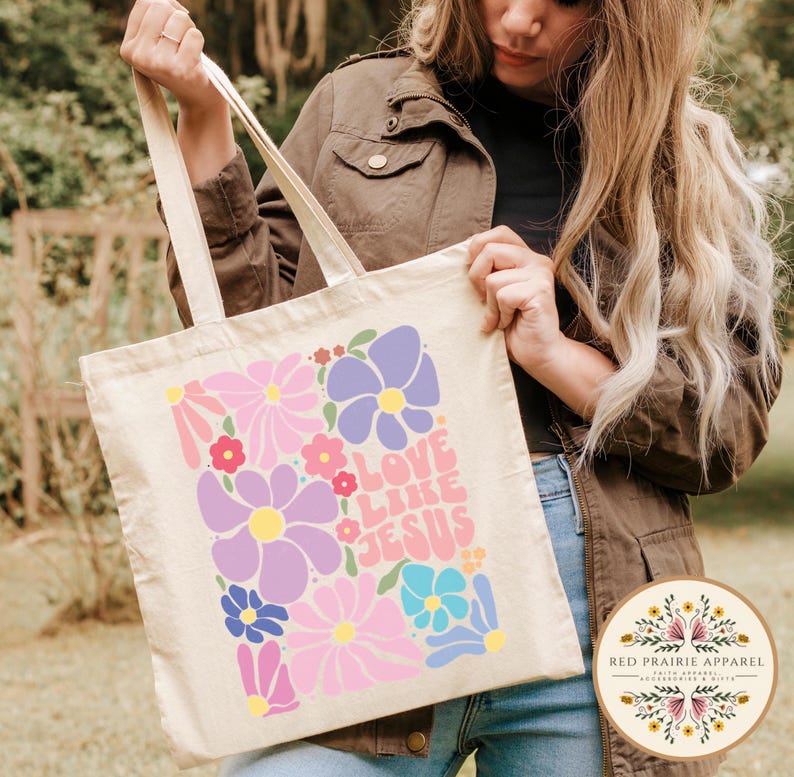 May include: A white canvas tote bag with a colorful floral design and the text "Love Like Jesus" in a retro font.