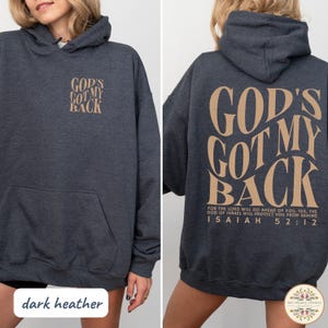 May include: Dark heather gray hoodie with the text "GOD'S GOT MY BACK" in a tan color on the front and back. The back also features a Bible verse. The hoodie has a front pocket and a hood.