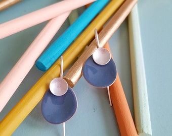 May include: A pair of silver and blue earrings with a simple, modern design. The earrings are made of metal and have a round, silver top with a blue, teardrop-shaped bottom.