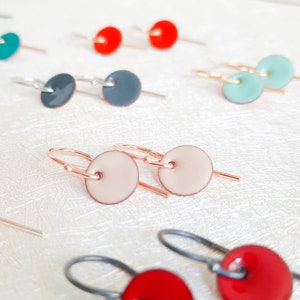Puede incluir: Un par de pequeños pendientes redondos de color rosa claro con ganchos de oro rosa. Los pendientes están hechos de cerámica y tienen un diseño simple y elegante.