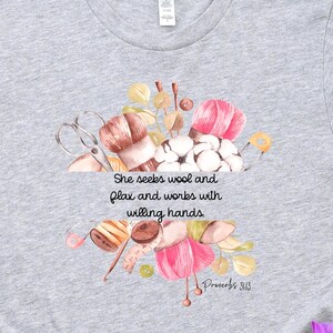 Proverbs 31:13 t shirt with images of pink, white and green knitting needles, crochet hooks, yarn and foliage.